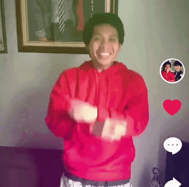 a man in a red hoodie is dancing in front of a framed picture .