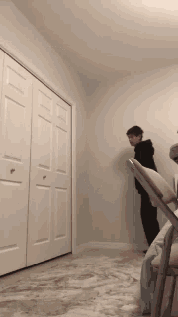 a man in a black hoodie is standing in a room next to a chair