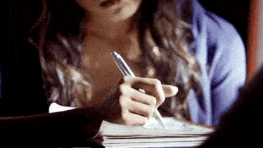 a woman is writing in a notebook while wearing a blue shirt