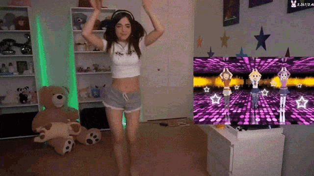 a girl is dancing in front of a tv with a teddy bear on the floor
