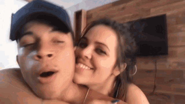a man and a woman are posing for a picture together . the woman is kissing the man on the neck .