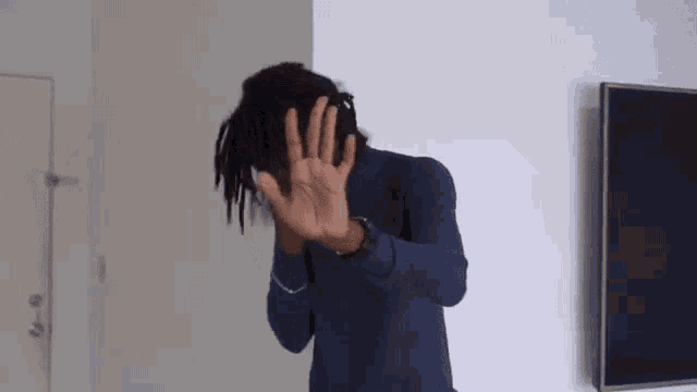 a man in a blue turtleneck is covering his face with his hands .