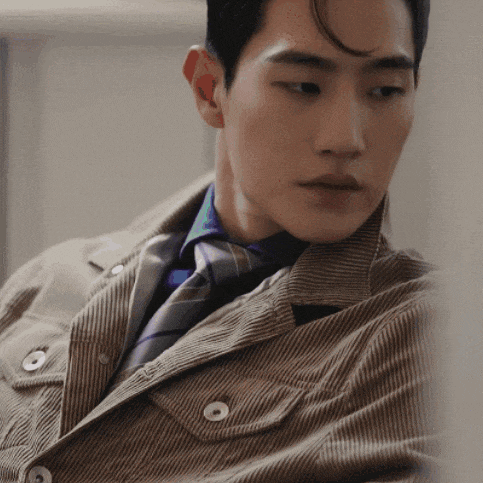 a man wearing a corduroy jacket and tie looks down