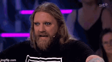 a man with long hair and a beard is wearing a black shirt with a white stripe on it .