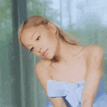 ariana grande is wearing a blue strapless dress with a bow on the shoulder and looking at the camera .