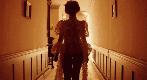 a woman in a long dress is walking down a hallway in a dark room .