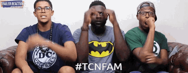 three men are sitting on a couch with one wearing a batman shirt