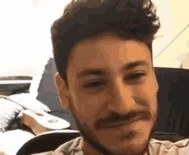 a man with a beard and mustache is sitting in a chair and smiling at the camera .