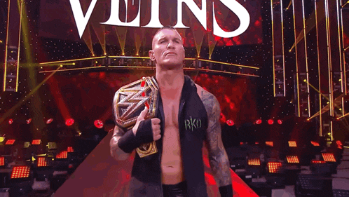 a wrestler with the word rko on his shirt is holding a wrestling championship belt