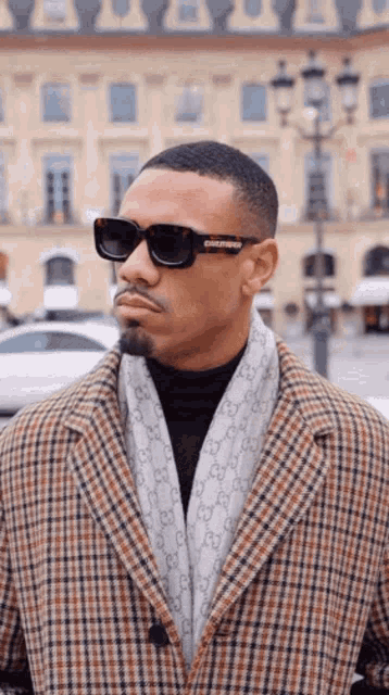 a man wearing sunglasses and a plaid coat with a scarf around his neck