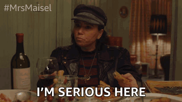 a woman sits at a table with a bottle of wine and a plate of food and says i 'm serious here