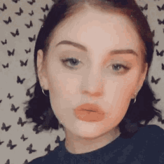 a woman is making a funny face in front of a wall with butterflies on it .
