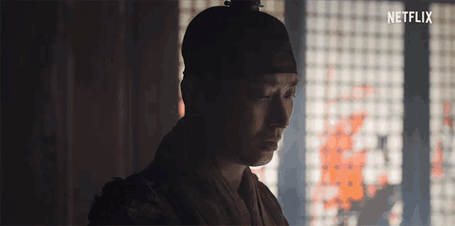 a man in a traditional costume is standing in front of a window with a fire in the background .