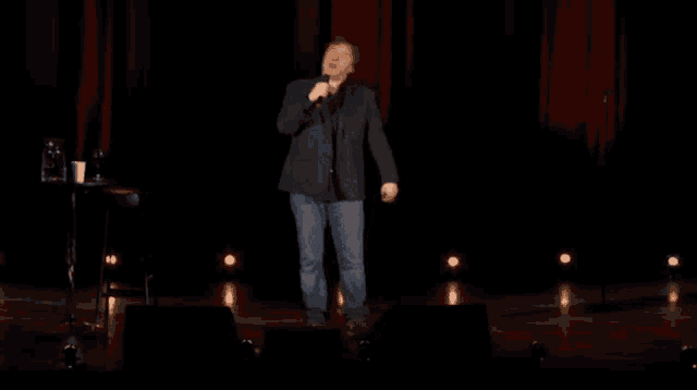 a man in a hat stands on a stage with a microphone