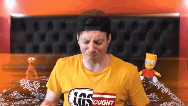 a man wearing a yellow shirt that says los tought is sitting on a bed