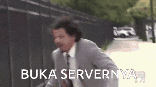 a man in a suit and tie is running down a street with the words `` buka servernya '' written on the screen .
