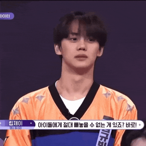 a young man wearing an orange shirt with stars on it stands in front of a purple background