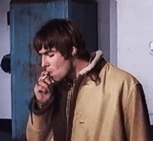 a man in a tan jacket is smoking a cigarette .
