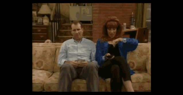 a man and a woman are sitting on a couch with a dog in the background