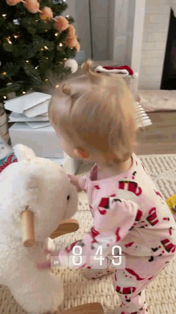 a baby is playing with a rocking sheep and the time is 8:49