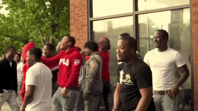 a group of men are standing in front of a building and one of them is wearing a red hoodie that says pla