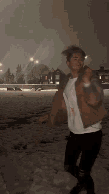a young man in a brown jacket is standing in the snow at night