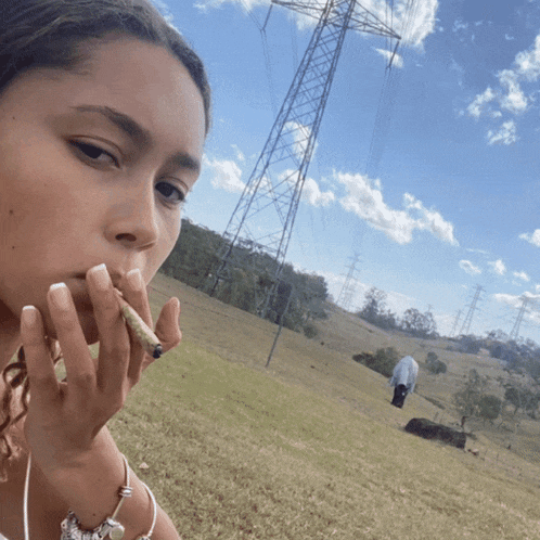 a woman smoking a cigarette in a field with power lines behind her