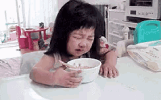 a little girl is sitting at a table with a bowl of cereal and a spoon .