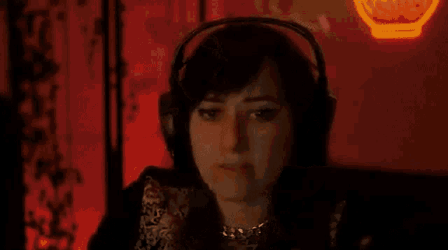 a woman wearing headphones is sitting in front of a neon sign in a dark room .
