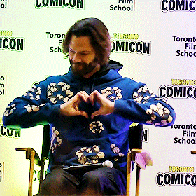 a man making a heart shape with his hands in front of a toronto comic con sign