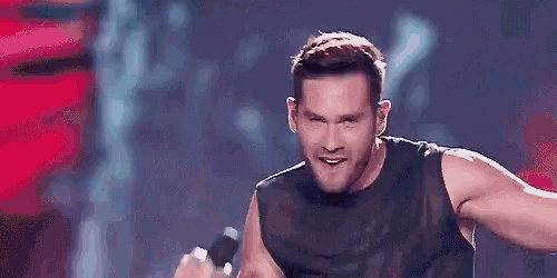 a man is standing on a stage wearing a black tank top .