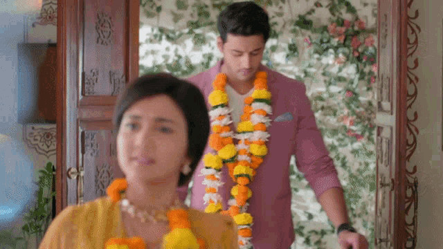 a man wearing a garland of flowers stands next to a woman in a yellow dress