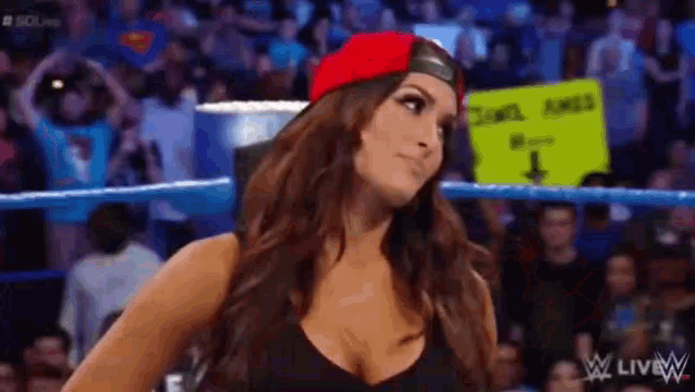 a woman is standing in a wrestling ring wearing a red hat and a black top .