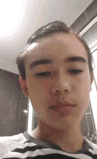a young man in a striped shirt is taking a selfie with his eyes closed .