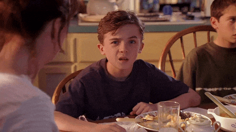a boy sitting at a table with a plate of food and a glass of water