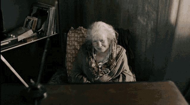 an elderly woman sits in a chair with a bookshelf behind her that has a picture of a woman on it