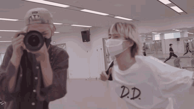 a man wearing a mask takes a picture of another man wearing a d.d. shirt