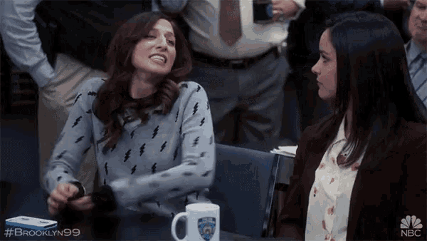 two women are sitting at a table with a brooklyn 99 mug on it