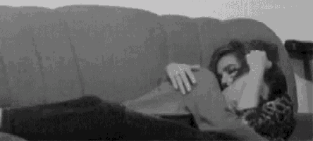 a black and white photo of a woman laying on a couch with a pillow .