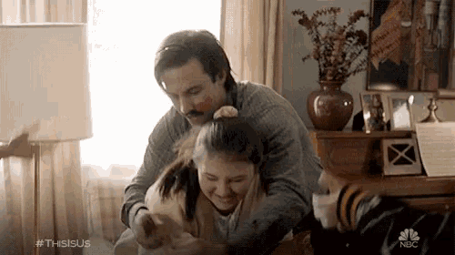 a man is putting a girl in a ponytail in a room with a vase of flowers in the background