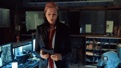 a woman in a black jacket holds a gun