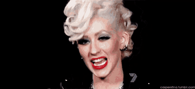 a close up of a woman with blonde hair and red lips smiling .