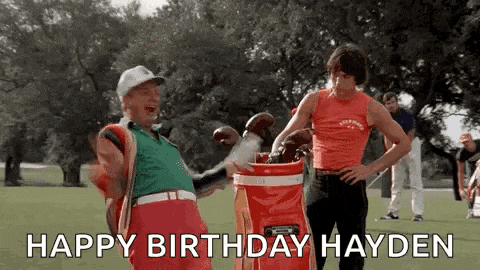 two men are standing next to each other on a golf course holding golf clubs and a golf bag .