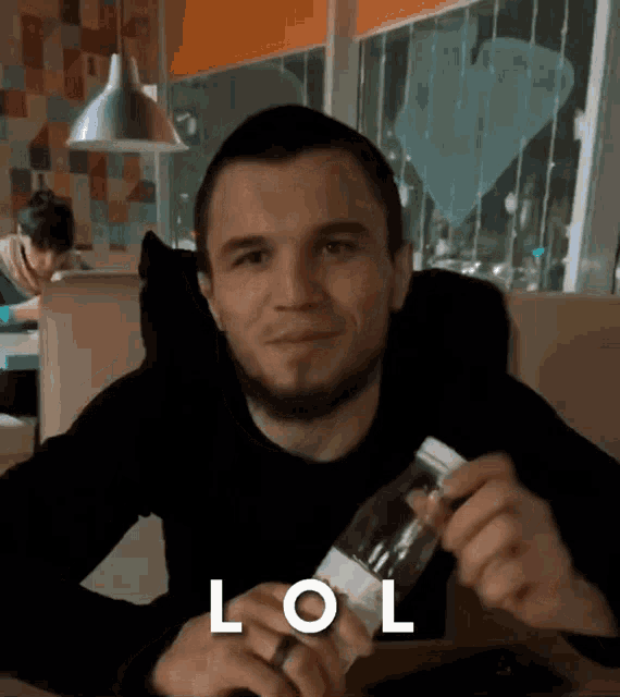a man sitting at a table holding a bottle of water with the word lol written on it