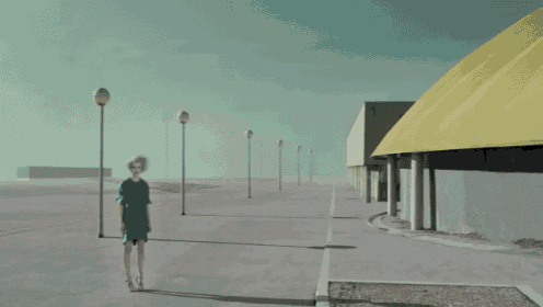 a woman in a green dress is walking down a sidewalk in front of a yellow building