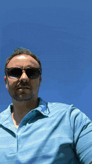 a man wearing sunglasses and a blue shirt with a blue sky in the background