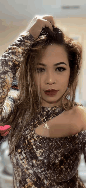 a woman wearing a snake print top holds her hair in her hand