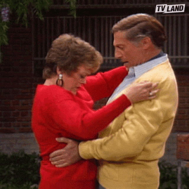 a woman in a red dress is hugging a man in a yellow sweater in front of a sign that says tv land