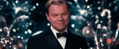 a man in a tuxedo and bow tie is smiling while standing in front of a crowd .