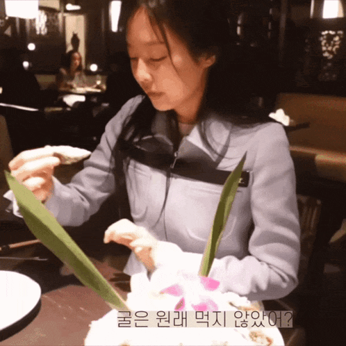 a woman is sitting at a table with a plate of food and a foreign language written on the bottom right corner